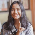 woman wearing gray crew-neck t-shirt smiling while making peace hand sign
